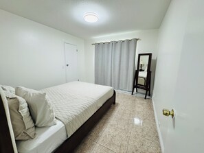 A bedroom with a bed, a door, a mirror, and a curtain. - Cozy 2-bedroom unit in central Westminster, Orange County. (Westminster)