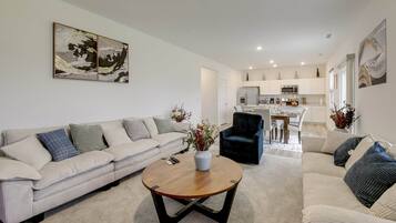 Ein modernes Wohnzimmer mit einer Couch, einem Couchtisch und einem Essbereich mit einer Küche im Hintergrund.