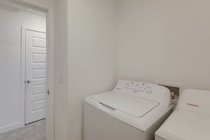 Ein Waschraum mit einer weißen Waschmaschine und einem Trockner, einer Tür und einem Lichtschalter an der Wand.