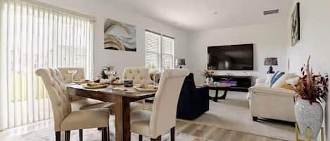 A dining area with a wooden table and chairs, a sofa, and a television in a living room.
