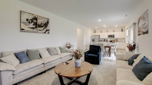 En moderne stue med sofa, sofabord og spiseplads med et køkken i baggrunden.