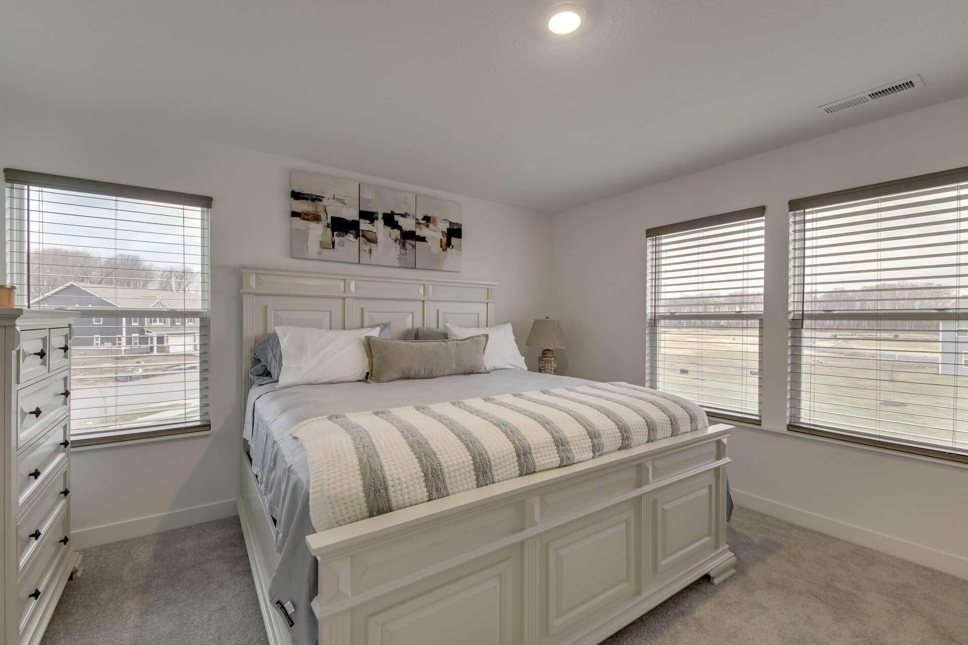 A bedroom with a large bed, a dresser, and a window with blinds.