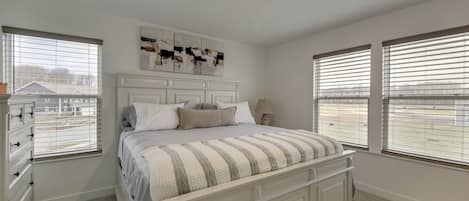A bedroom with a large bed, a dresser, and a window with blinds.
