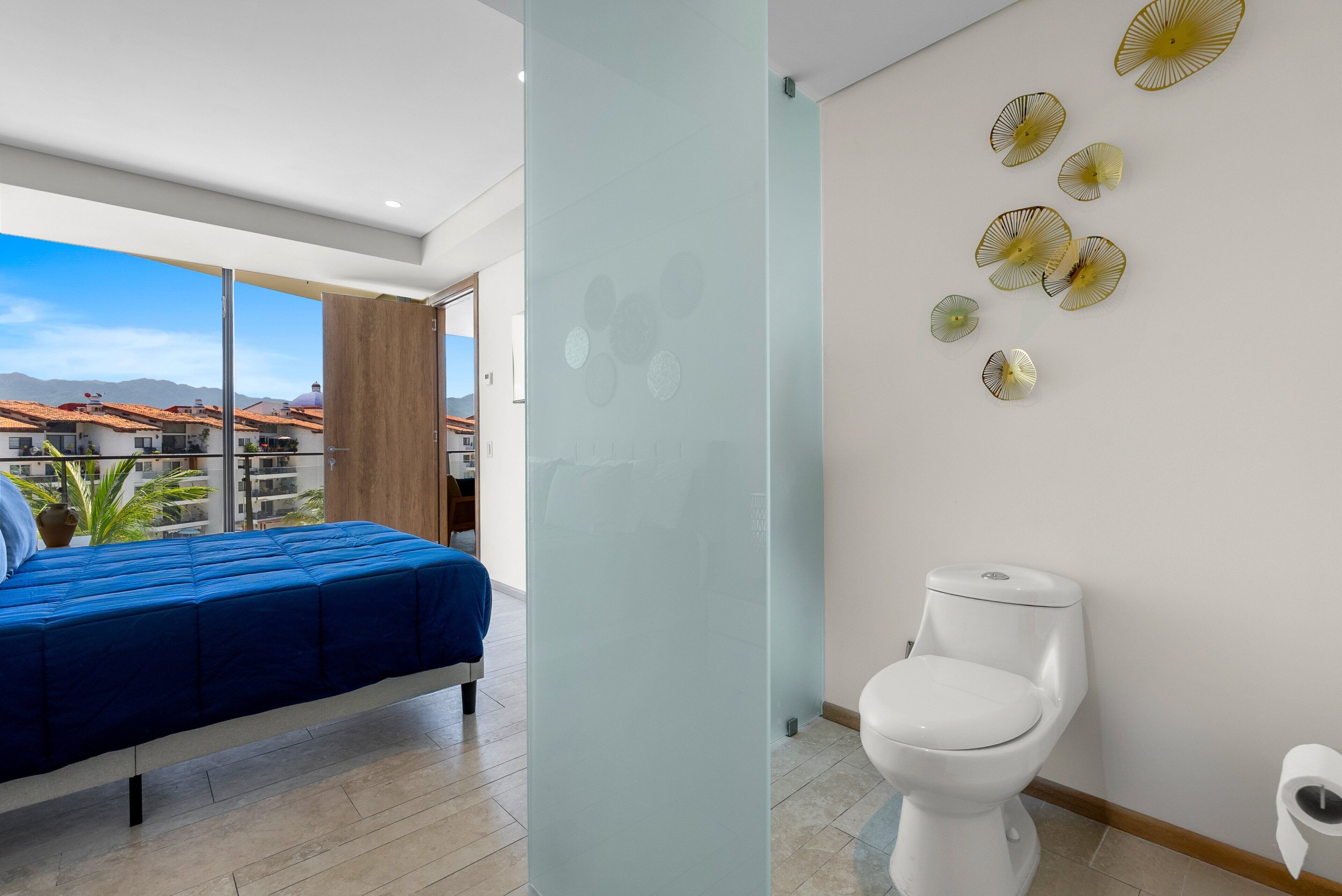 A modern hotel room with a bed, a toilet, and a balcony with a view of buildings.