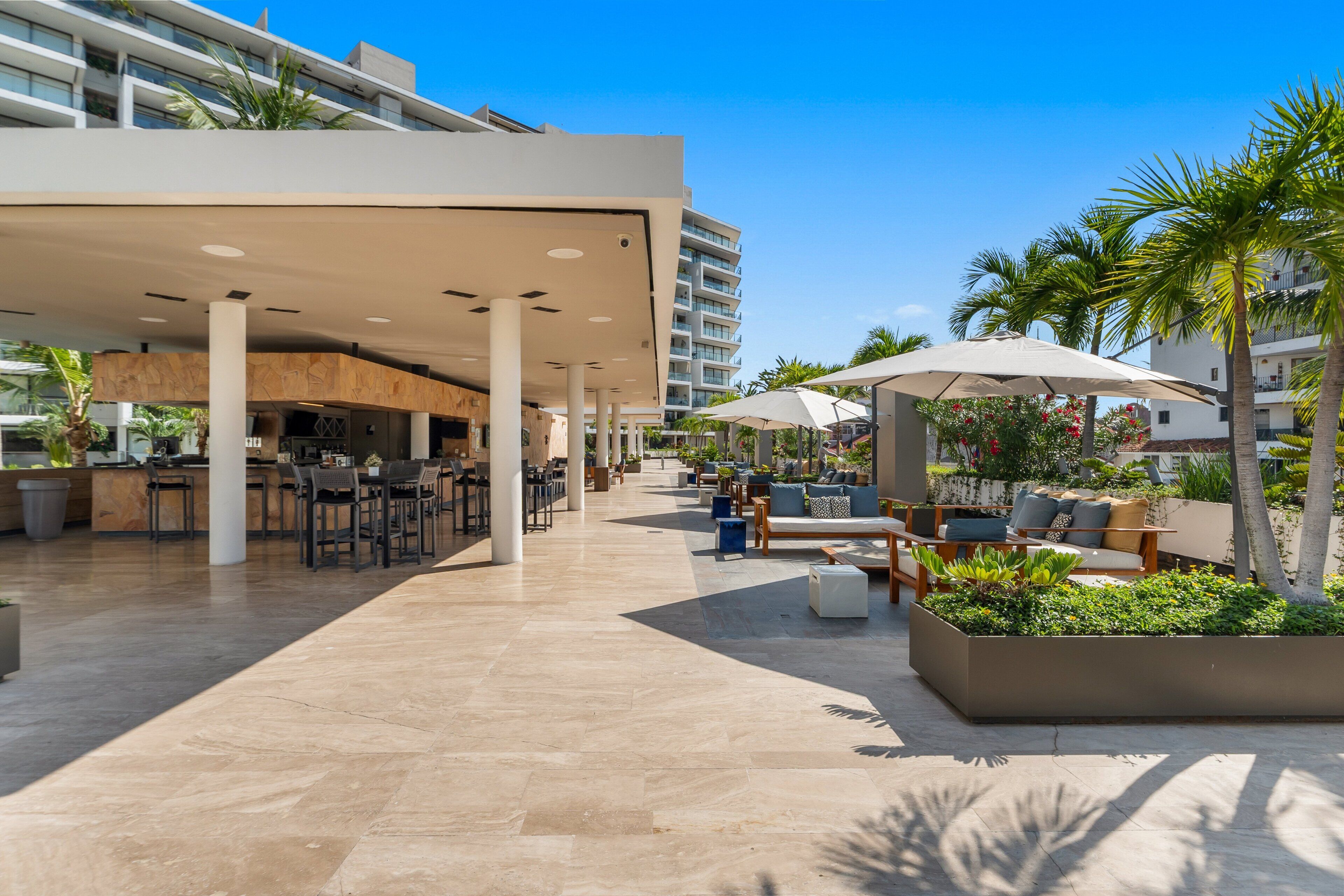 A modern outdoor area with a bar, seating, and palm trees.
