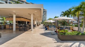 A modern outdoor area with a bar, seating, and palm trees.