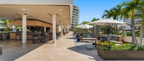 A modern outdoor area with a bar, seating, and palm trees.