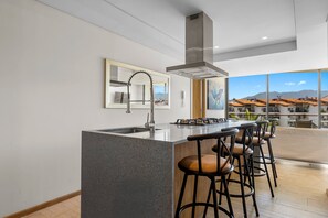 A modern kitchen with a central island, bar stools, a stainless steel range hood, and a large window offering a view of buildings and mountains. - 1BR, 2BA condo in Marina Vallarta, Puerto Vallarta. (Puerto Vallarta)