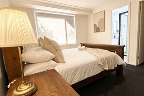 A bedroom with a bed, a bedside lamp, a window, and a door. - Casa Oliva | Spacious Retreat Near Toranga Zoo (Dubbo)