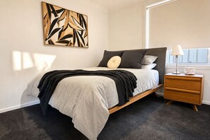 A bedroom with a bed, bedside table, lamp, and abstract artwork on the wall. - Casa Oliva | Spacious Retreat Near Toranga Zoo (Dubbo)