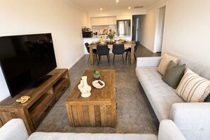 Un salon moderne avec un téléviseur à écran plat, une table basse en bois et un canapé gris.