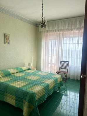 A room with a bed, a chair, a chandelier, and a window with curtains. - VILLA MARELUCE (Santa Marinella)