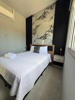 Een hotelkamer met een bed, nachtkastje, lamp, marmeren muur en raam.