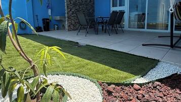 Een moderne patio buiten met gazon, zitgedeelte en een stenen muur.