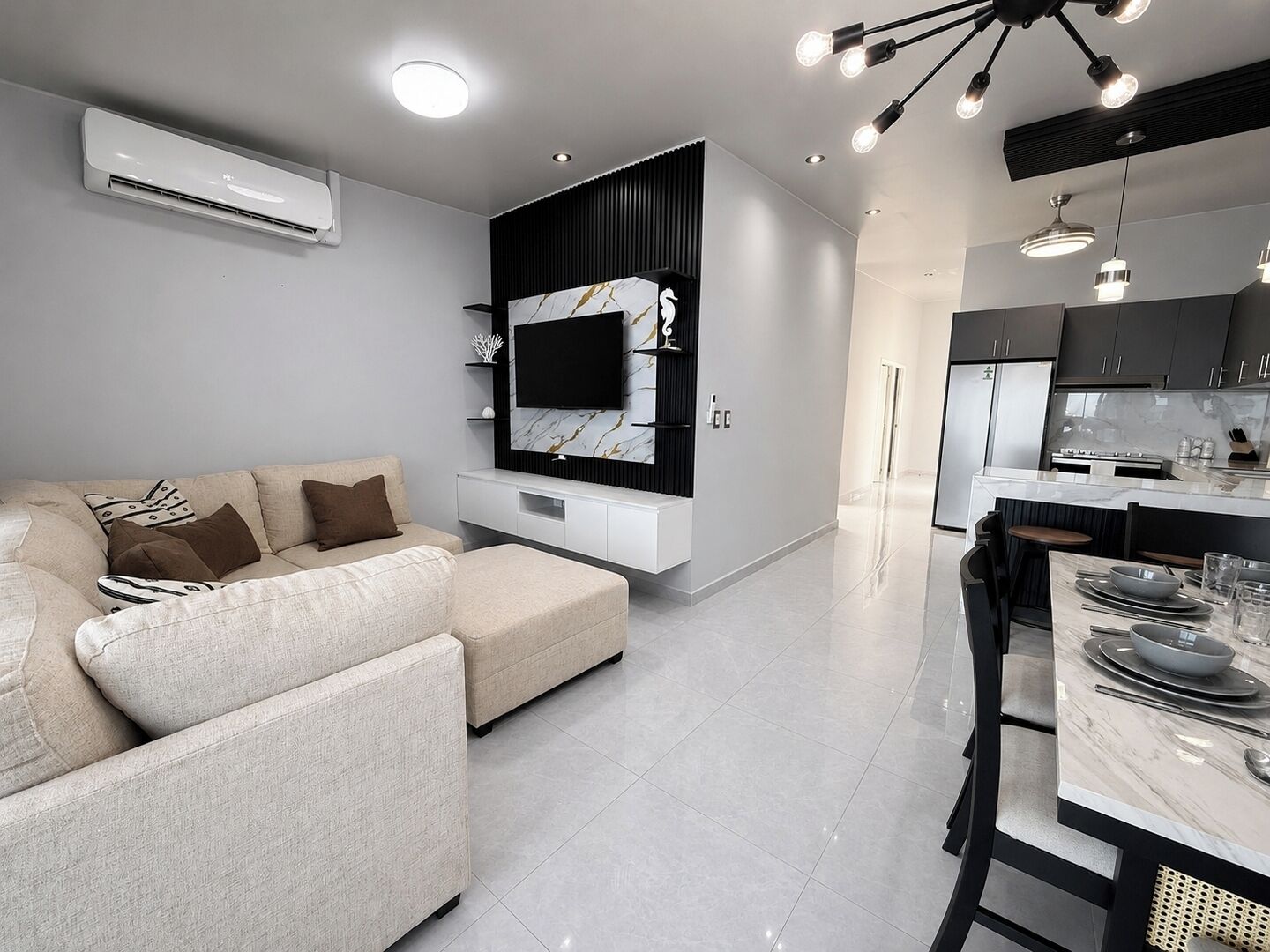 Una sala moderna con un sofá, un televisor de pantalla plana y una zona de comedor con una mesa preparada para dos.