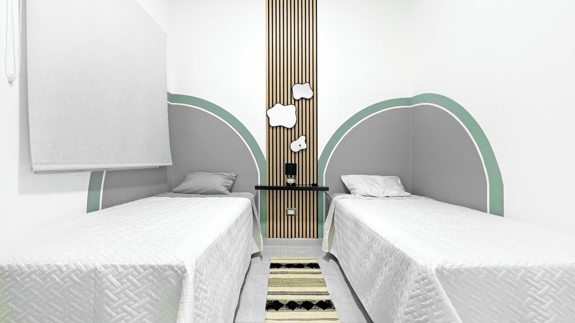 Una habitación con dos camas individuales, una mesita y un estante en la pared.