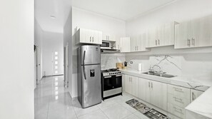 Una cocina moderna con electrodomésticos de acero inoxidable, armarios blancos y piso de baldosas.