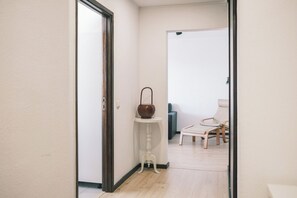 Ein Flur mit einer weißen Tür, einem kleinen weißen Tisch mit einem braunen Topf, einem Stuhl und einem Sofa.