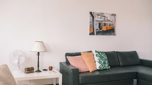 En stue med en sort lædersofa, et hvidt sengebord med en lampe, en ventilator og en lille pyntegenstand.