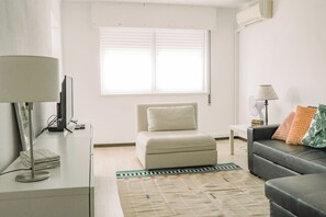 Ein modernes Wohnzimmer mit einer Couch, einem Sessel, einer Lampe und einem Fernseher.