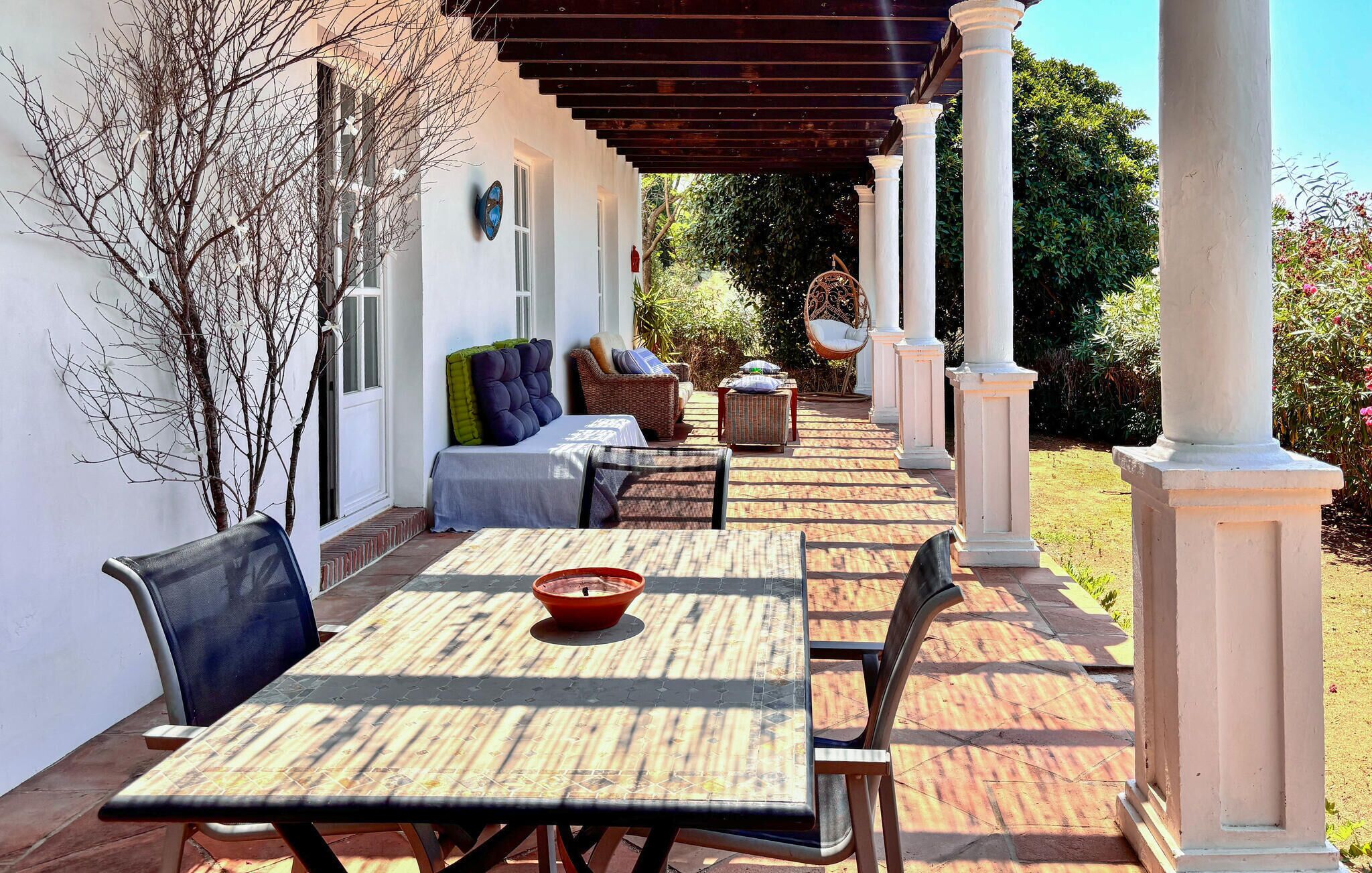 Une terrasse couverte avec une table et des chaises, un canapé et un fauteuil décoratif.