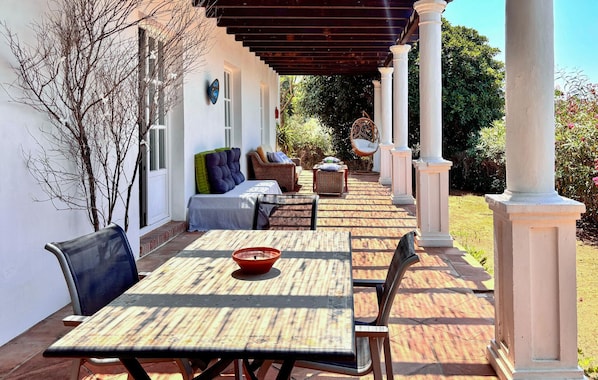A covered patio with a table and chairs, a sofa, and a decorative chair.
