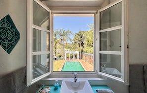 A bathroom with a window view of a pool and a white structure.