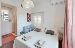 A bedroom with a bed, a hanging light fixture, a wall-mounted air conditioner, and a window with curtains.