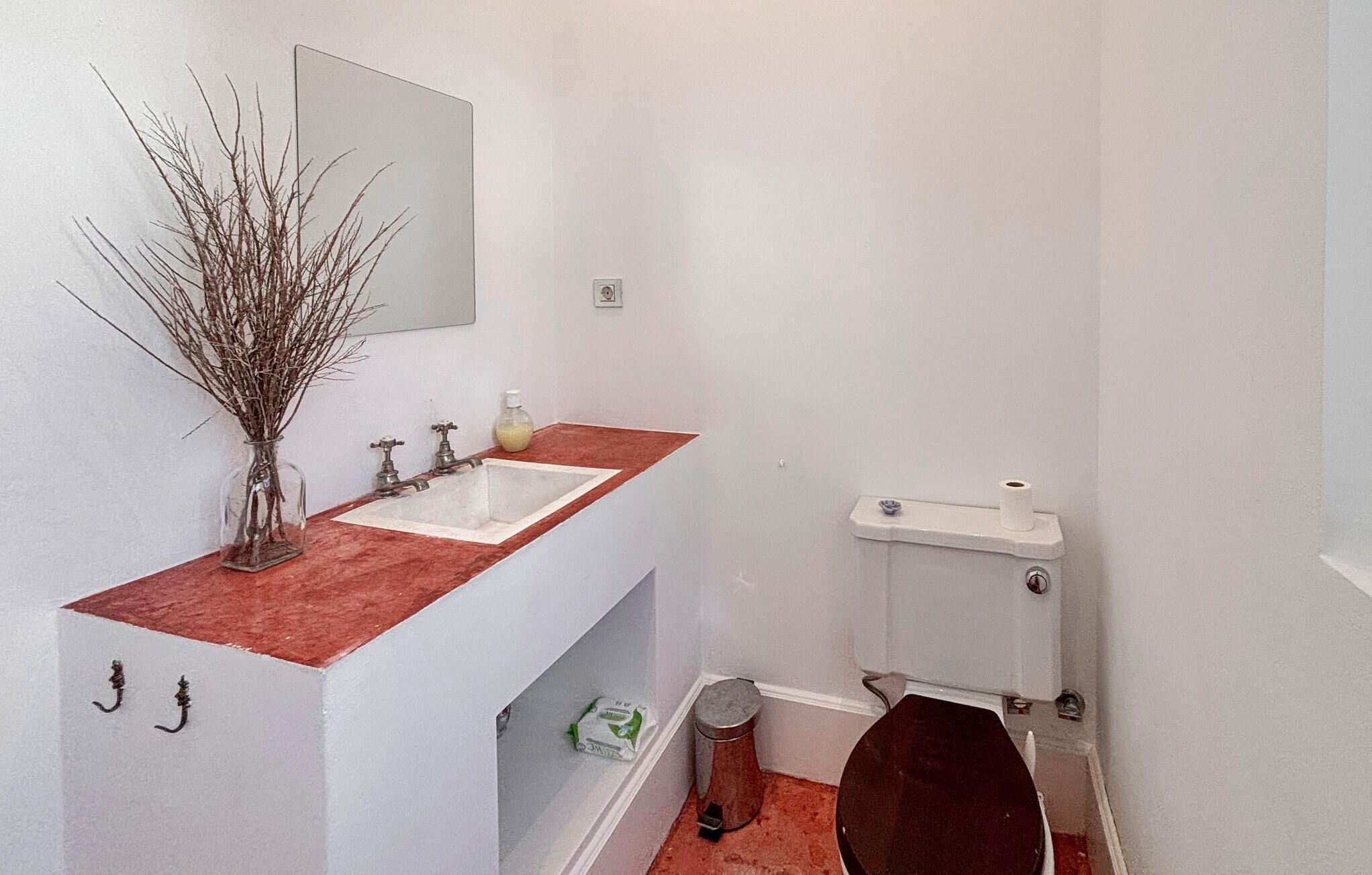 A bathroom with a white sink, a mirror above it, a toilet, and a trash can.
