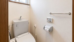 A small, clean bathroom with a toilet, a hand dryer, a paper towel dispenser, and a window with a towel rail. - Asahikawa Family Stay KT (Asahikawa)
