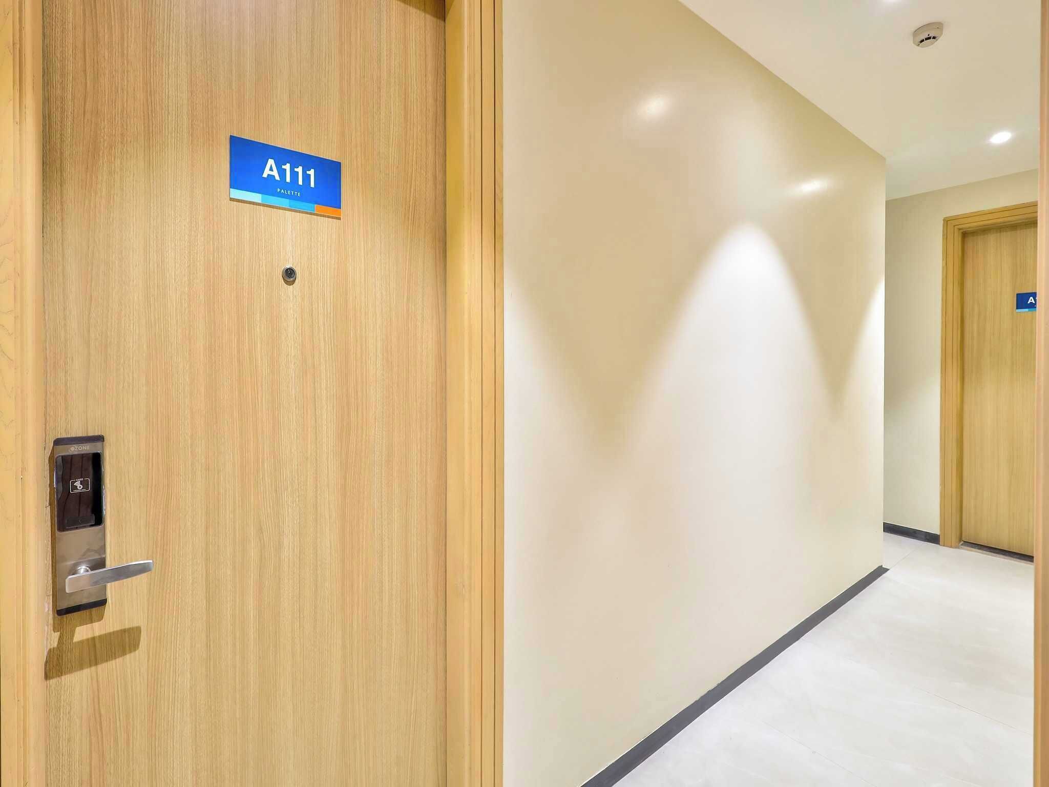 Un pasillo con una puerta de madera identificada con la etiqueta 'A111' y un letrero azul que indica una 'PALETTE' de servicios.