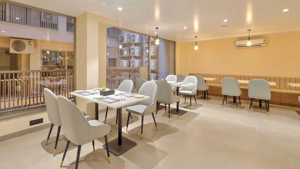 A modern dining area with tables and chairs, air conditioning units, and a view of the outside. - Palette Hotel Millennium City Gurugram (Gurugram)