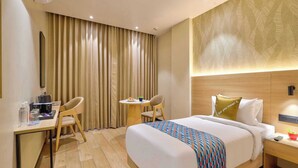 A hotel room with a bed, a desk, two chairs, a small table, and a nightstand. - Palette Hotel Millennium City Gurugram (Gurugram)