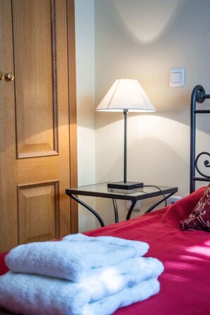 Ein Hotelzimmer mit Holztür, Nachttisch mit Lampe, Bett mit roter Decke und rotem Kopfkissen.