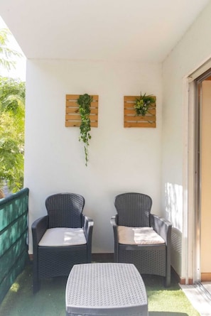 Ein Balkon mit zwei Korbstühlen, einem kleinen Tisch und zwei wandmontierten Holzplanzen mit Grünpflanzen.