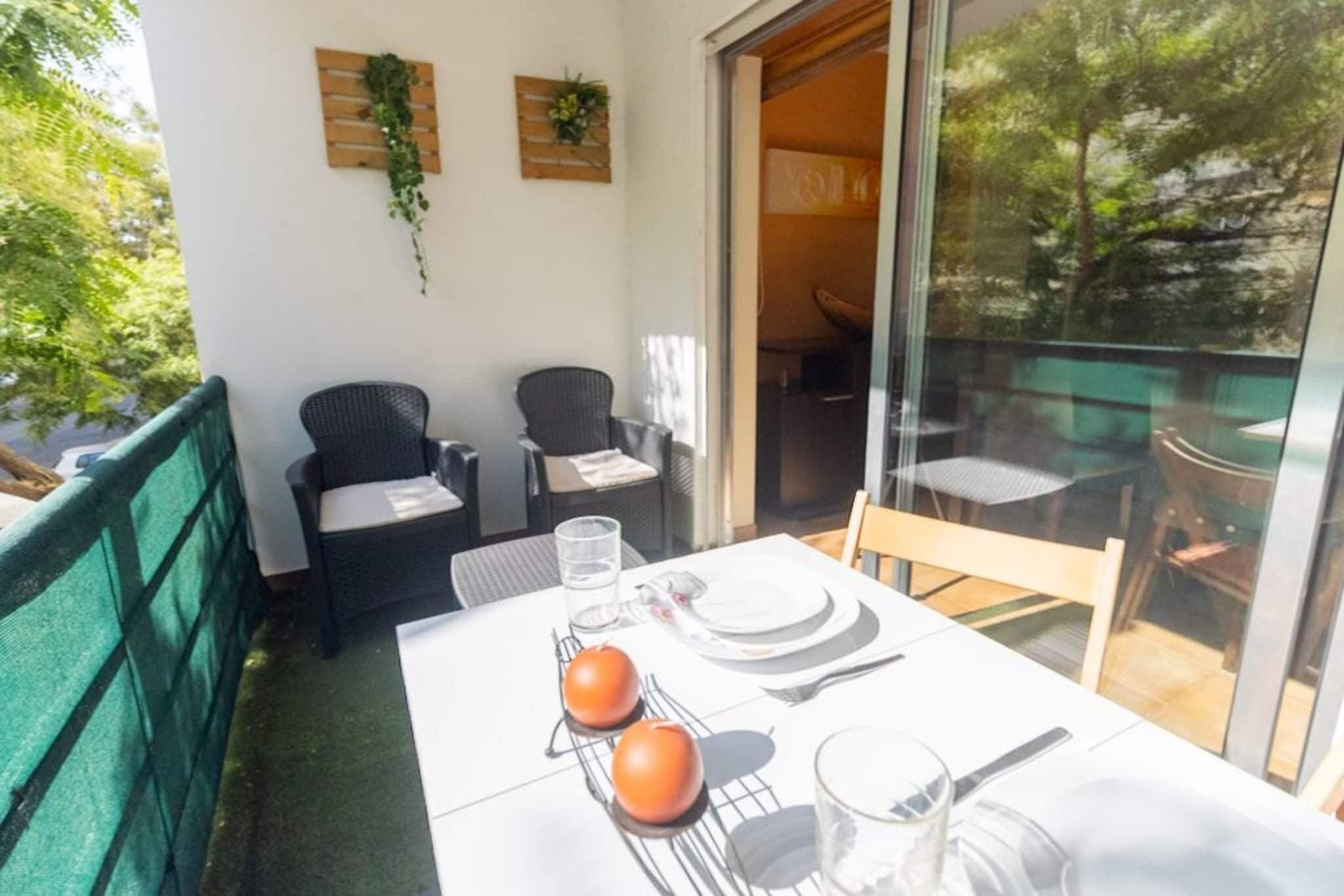 A balcony with a table set for two, two wicker chairs, a glass of water, and a plate with two tomatoes.