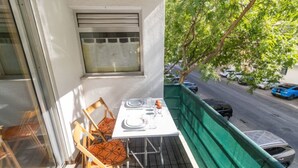 A balcony with a table set for two, chairs, and a view of the street.