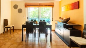 A dining area with a table and chairs, a window with blinds, a decorative wall piece, and a cabinet with drawers.