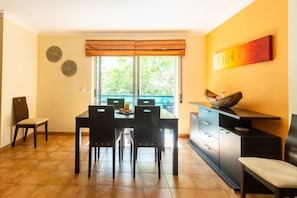 A dining area with a table and chairs, a window with blinds, a decorative wall piece, and a cabinet with drawers.