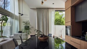 A modern kitchen with a central island, wooden cabinets, and a dining area with a table and chairs. - Nexa Townhouse 08 (Badung)