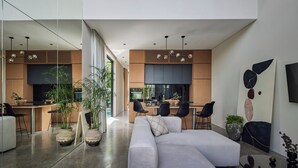 A modern interior with a large L-shaped sofa, a dining area with chairs, and a kitchen with wooden cabinets. - Nexa Townhouse 08 (Badung)