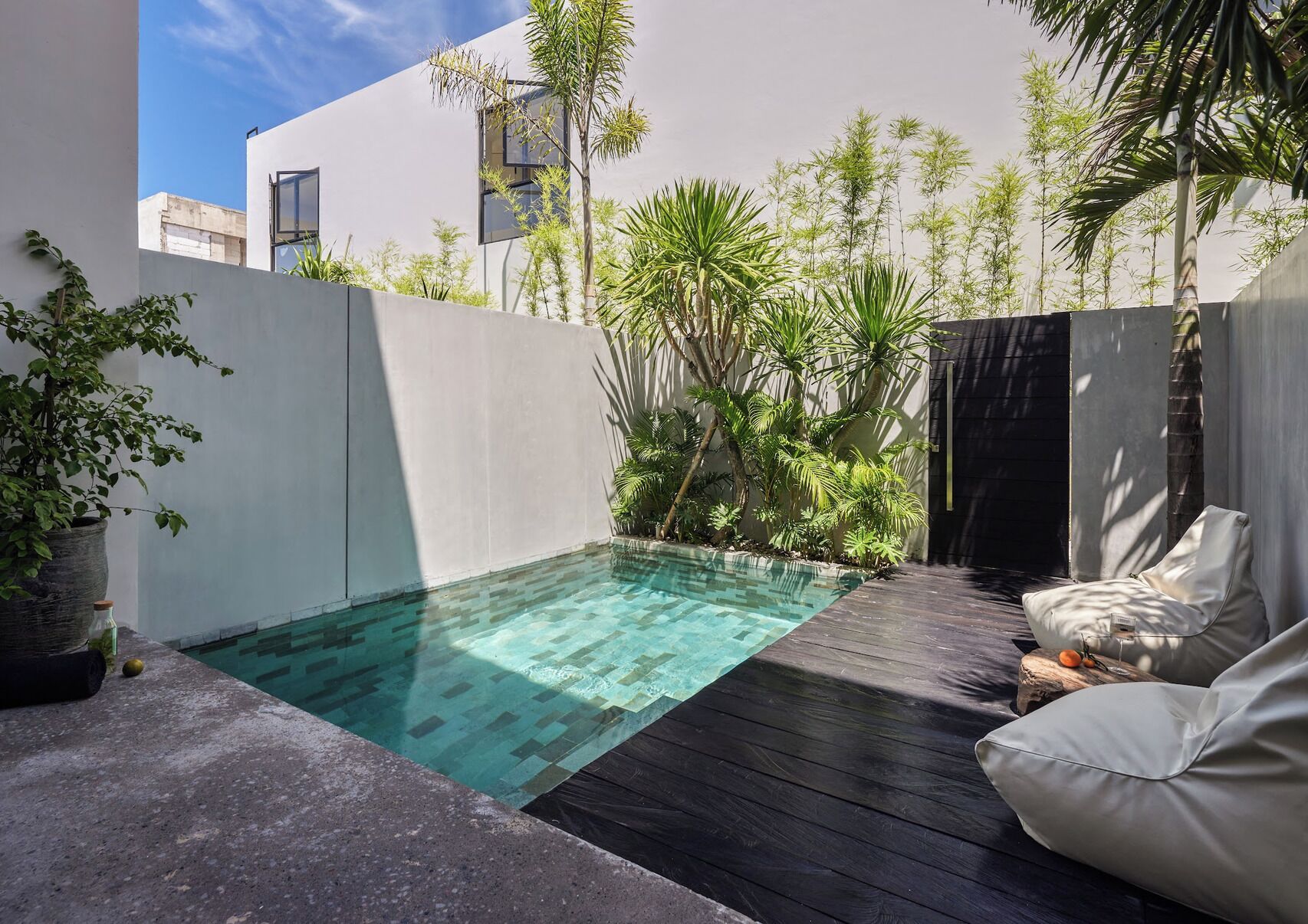 Un área de piscina moderna al aire libre con cubierta de madera y pared blanca.