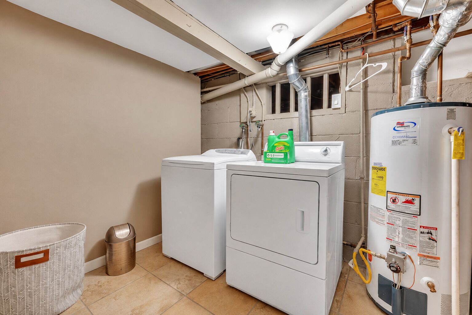 A laundry room with two washers and dryers, a water heater, and a metal trash can.