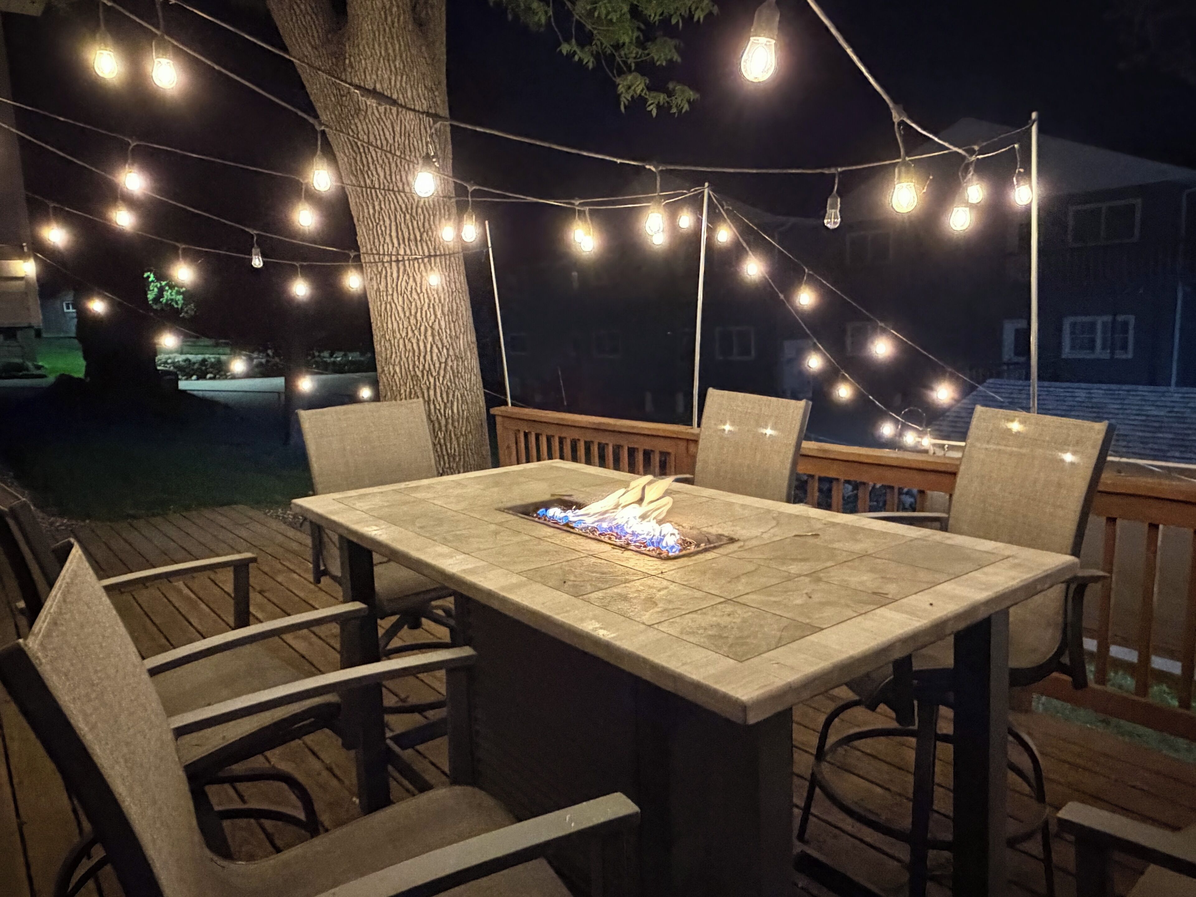 Un área de comedor al aire libre con una mesa y sillas, rodeada de luces colgantes.