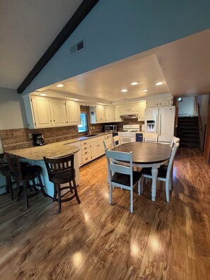 A spacious kitchen with a central island, wooden flooring, and white cabinetry.