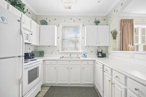 A kitchen with white cabinets, a stove, a microwave, and a window with blinds. - Cozy 2-bedroom condo with AC in charming North Myrtle Beach (North Myrtle Beach)