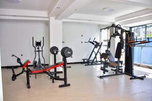 A gym with various exercise equipment, including a bench press, squat rack, and weight bench. - Modern 1BDRM Apartment|Kilimani|Fast WiFi and Cool views of Nairobi (Nairobi)
