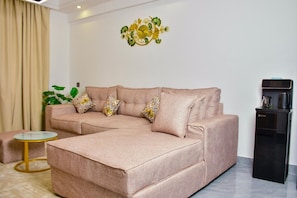A living room with a sofa, a coffee machine, and a decorative wall piece. - Modern 1BDRM Apartment|Kilimani|Fast WiFi and Cool views of Nairobi (Nairobi)