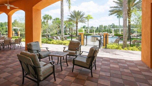 A covered patio area with outdoor seating, a pool, and palm trees in the background. - Luxury Getaway 4 Bd/5 Bath 25 Mins to DisneyMagic! (Davenport)