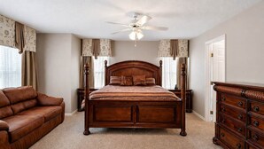 A bedroom with a wooden bed, a leather sofa, a dresser, and a ceiling fan. - Luxury Getaway 4 Bd/5 Bath 25 Mins to DisneyMagic! (Davenport)